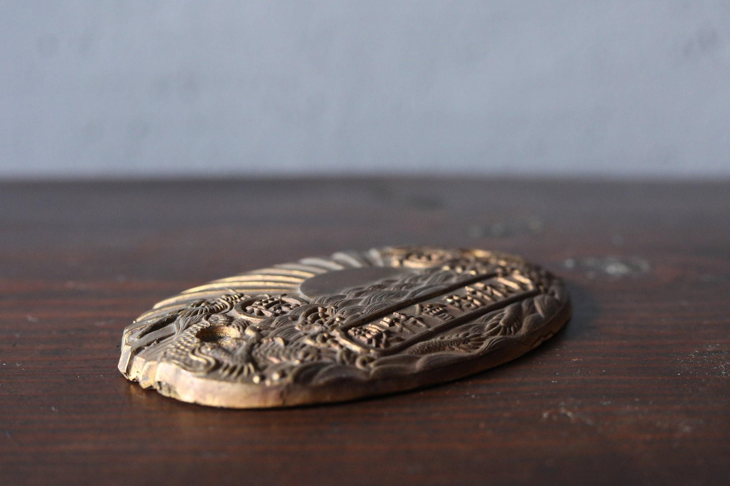 a close-up view of a decorative metal object, possibly a badge or plaque, resting on a wooden surface.
