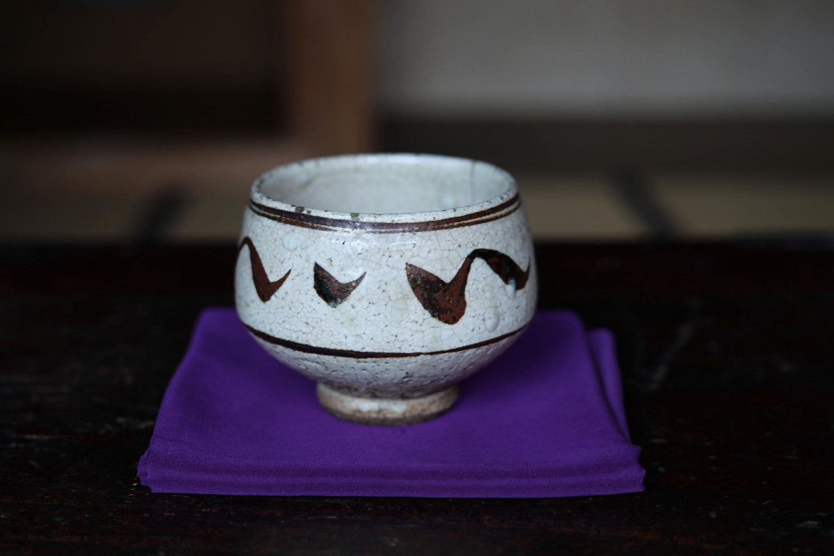 A white ceramic bowl with a decorative design sits on a purple cloth on a wooden surface.