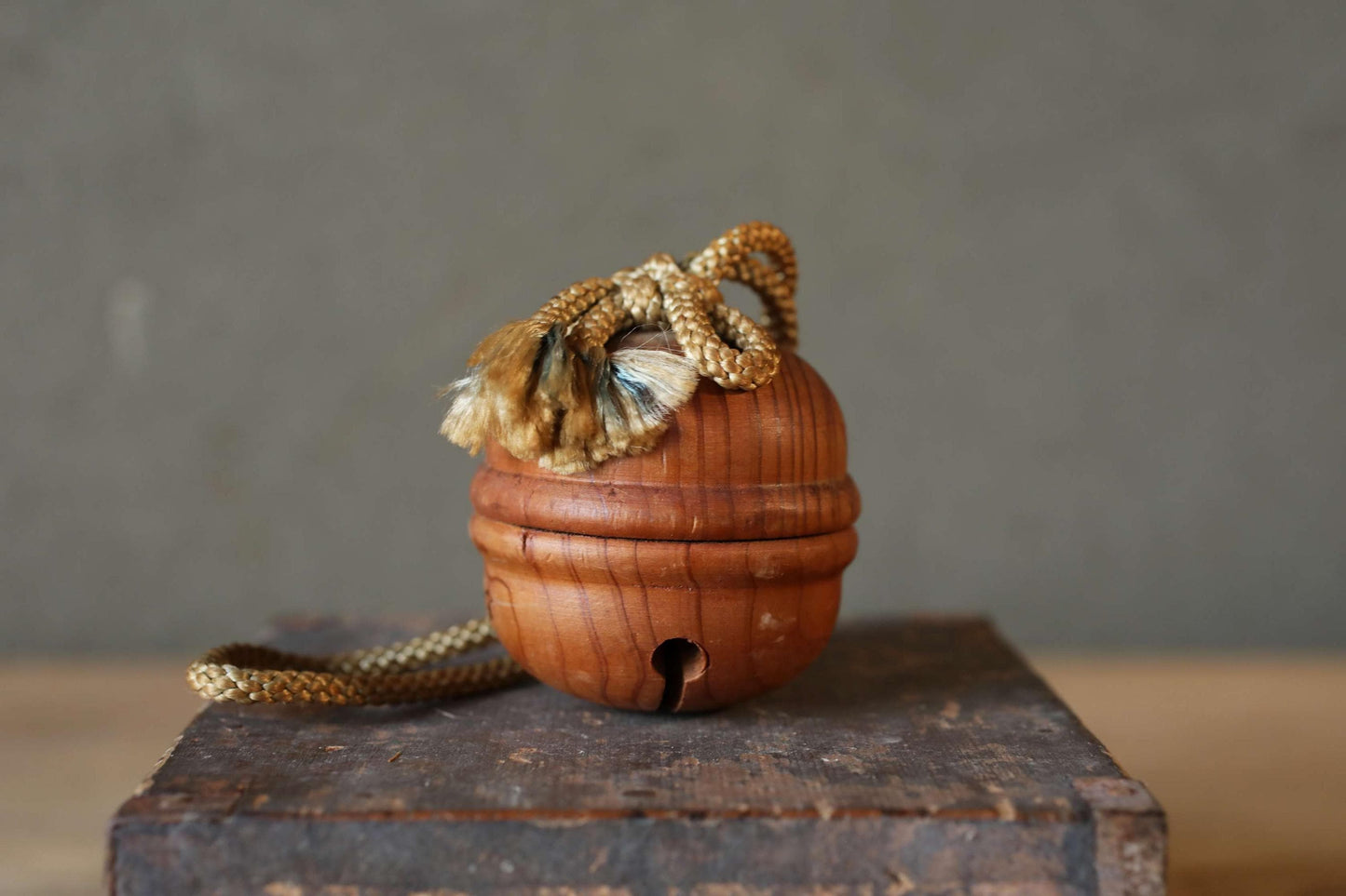 A wooden bell with a tassel hanging from it, placed on a wooden surface against a gray background.