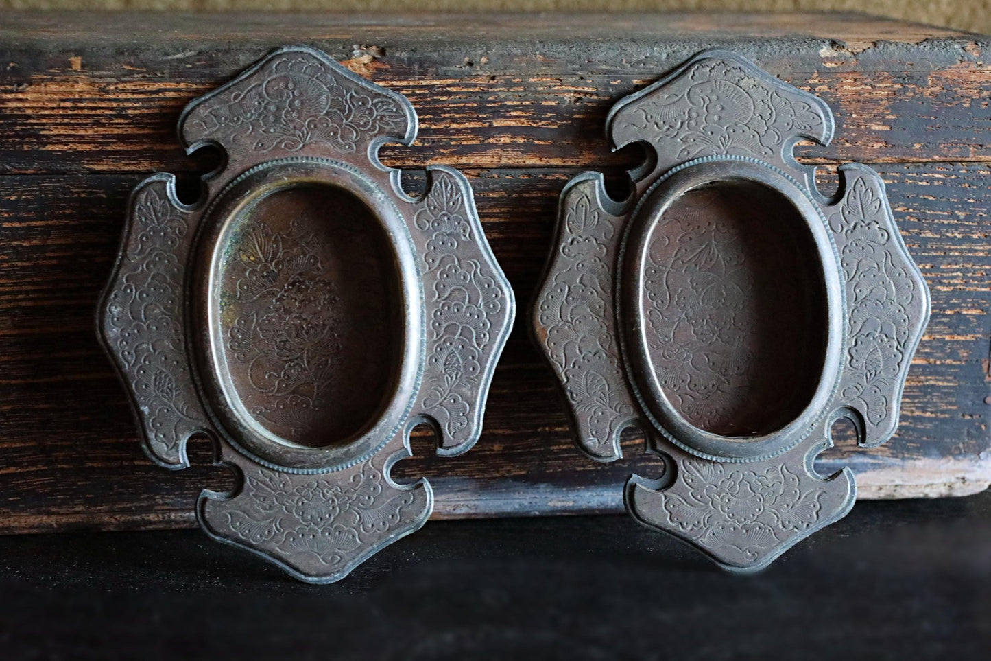 two ornate metal picture frames with intricate designs, placed on a wooden surface.