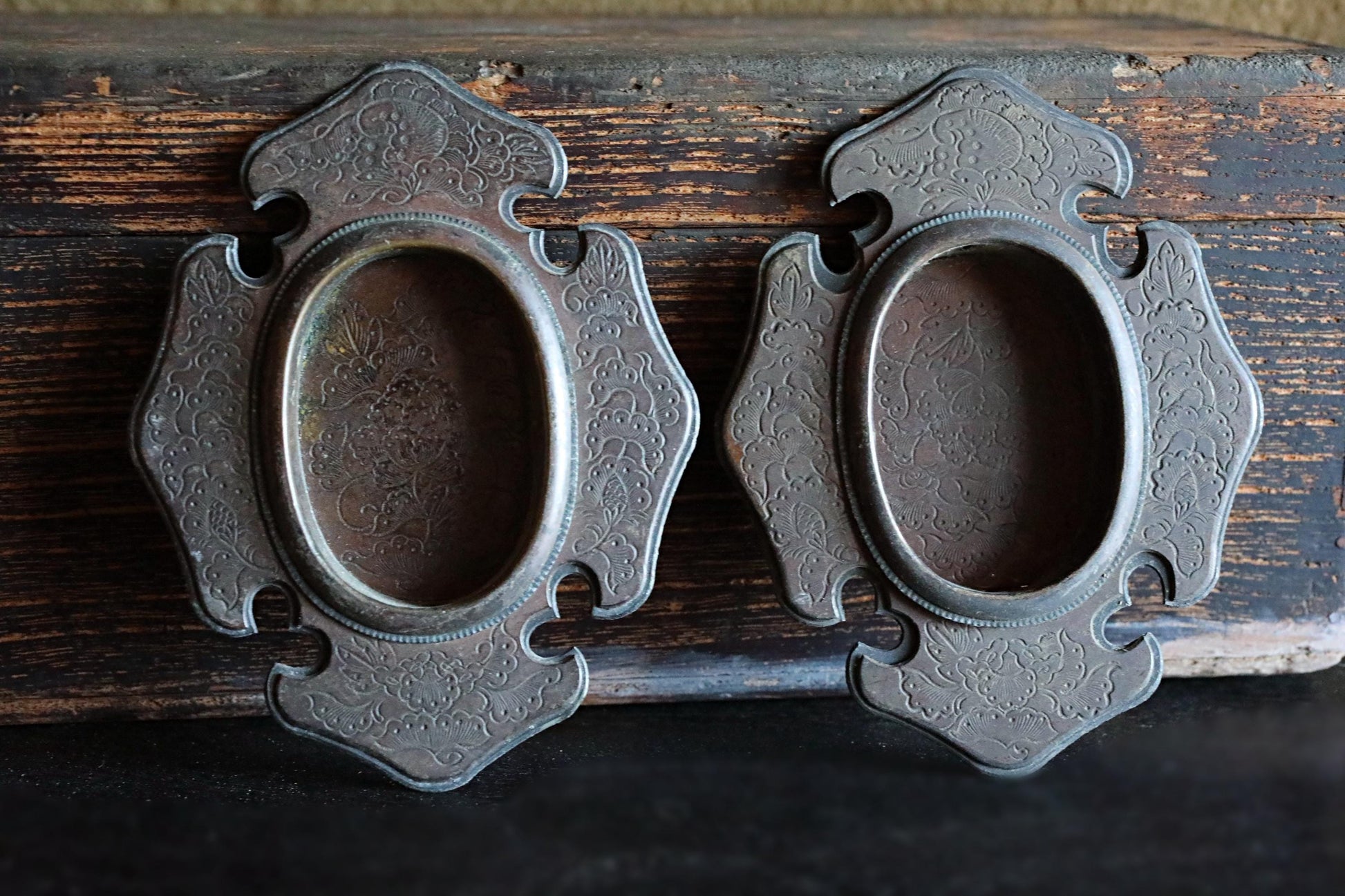 two ornate metal picture frames with intricate designs, placed on a wooden surface.