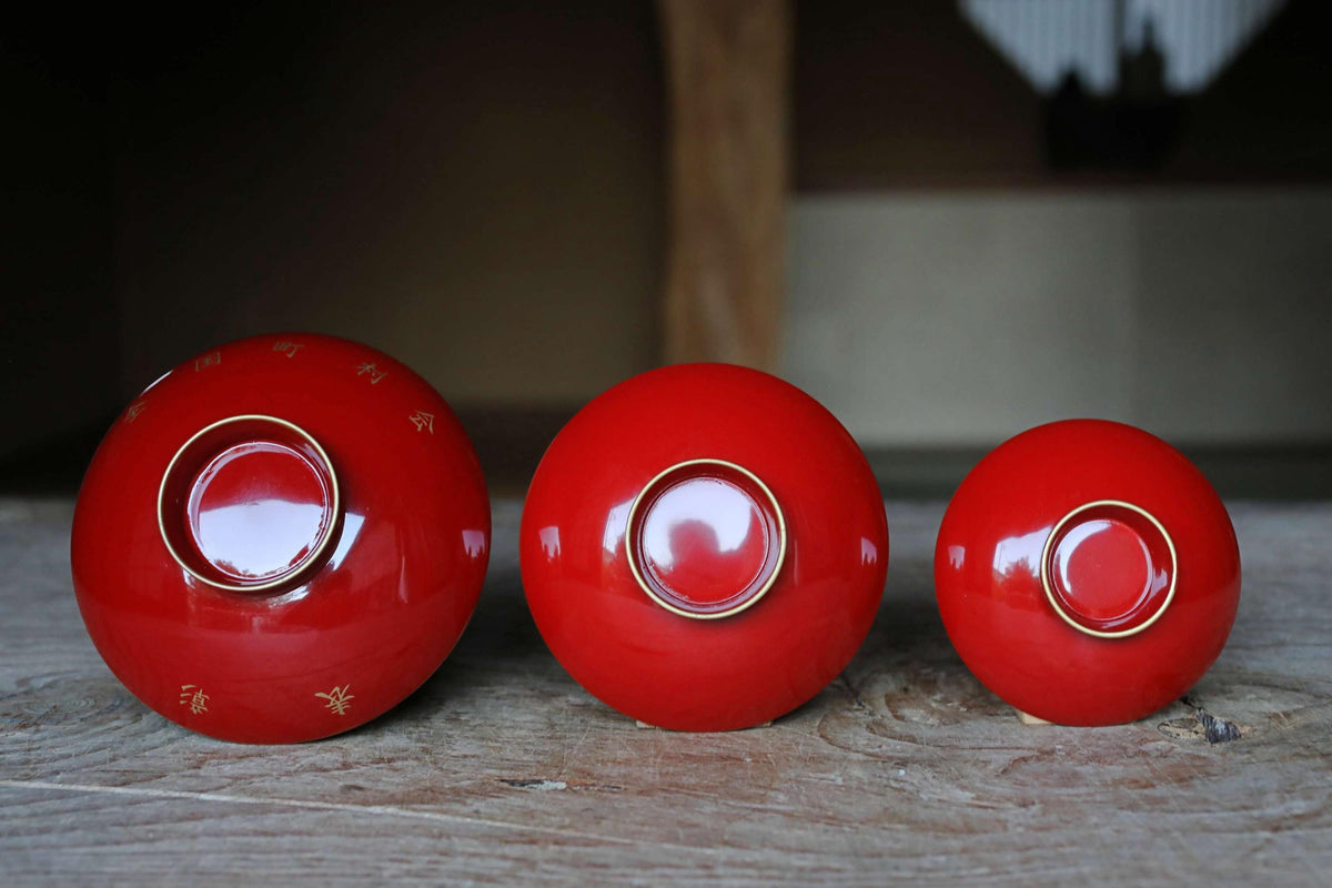 Three red bowls with gold accents are arranged in a row on a wooden surface.