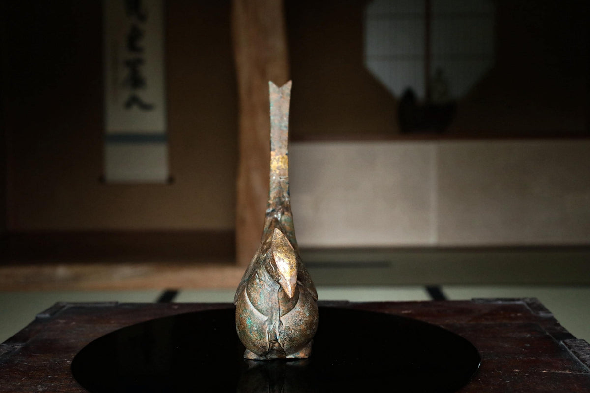 a small, ornate vase or sculpture with a tall, slender shape and a pointed top, placed on a black circular surface.