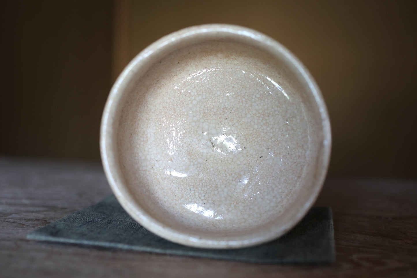 A white ceramic bowl with a speckled texture sits on a dark surface, possibly a piece of cloth or a coaster.