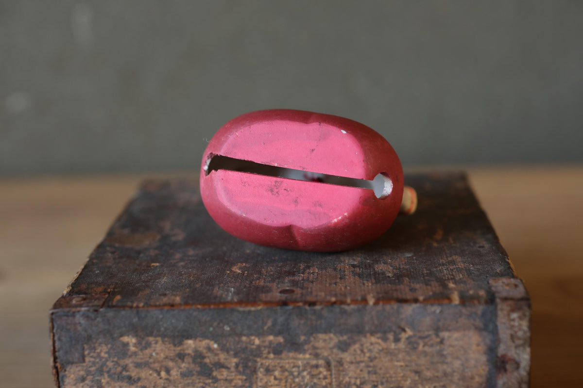 A red metal bell with a hole in the middle is sitting on a wooden surface.