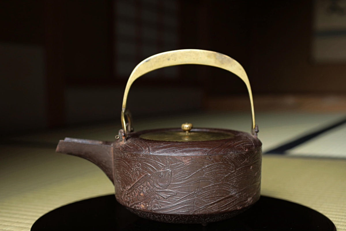 A dark brown, intricately designed teapot with a gold handle and lid sits on a black surface.