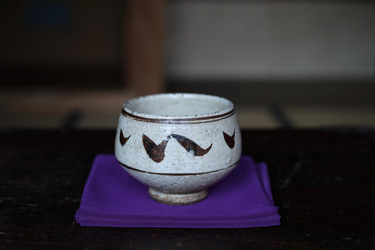 A white ceramic bowl with black designs sits on a purple cloth on a dark wooden surface.