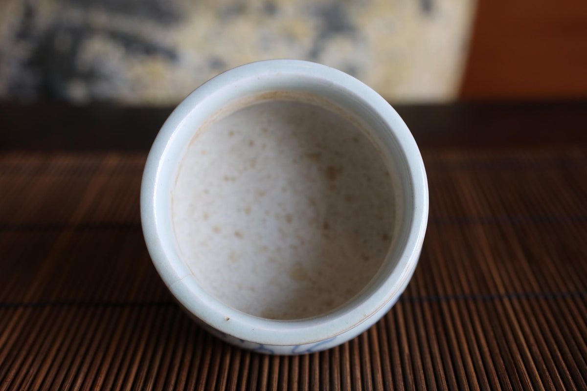 A white ceramic bowl with a blue pattern sits on a bamboo mat, with a blurred background.