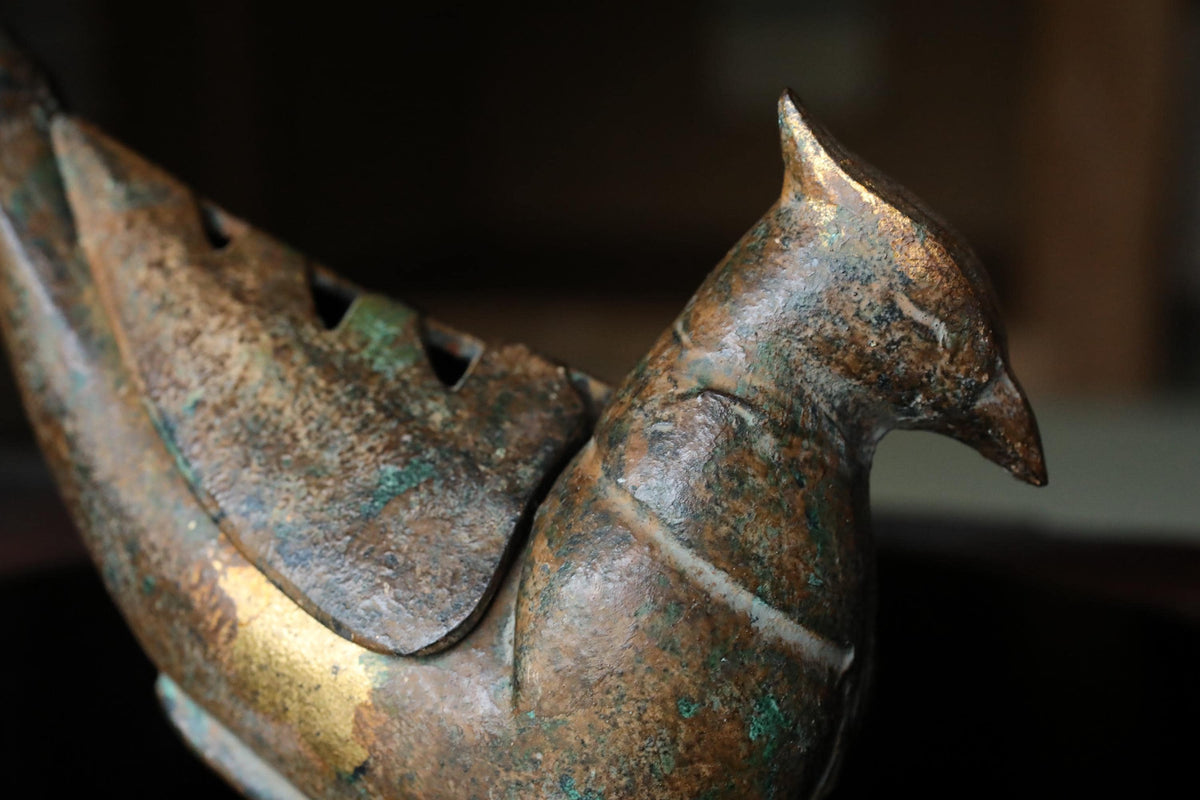 A close-up view of a bronze bird figurine, with a textured and weathered appearance.