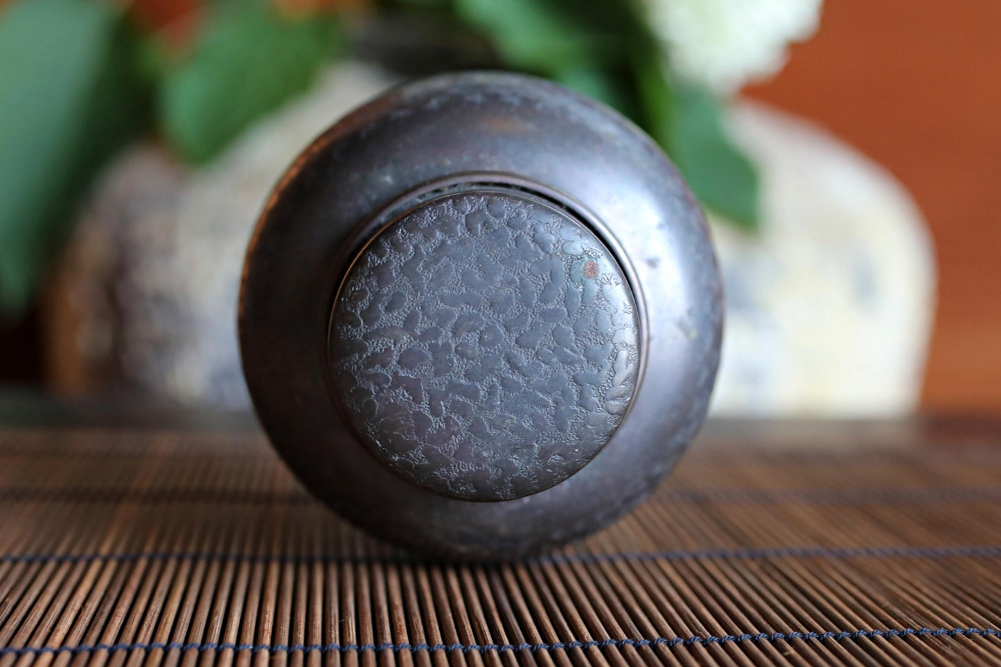 A close-up view of a dark metal container with a textured surface, placed on a bamboo mat.