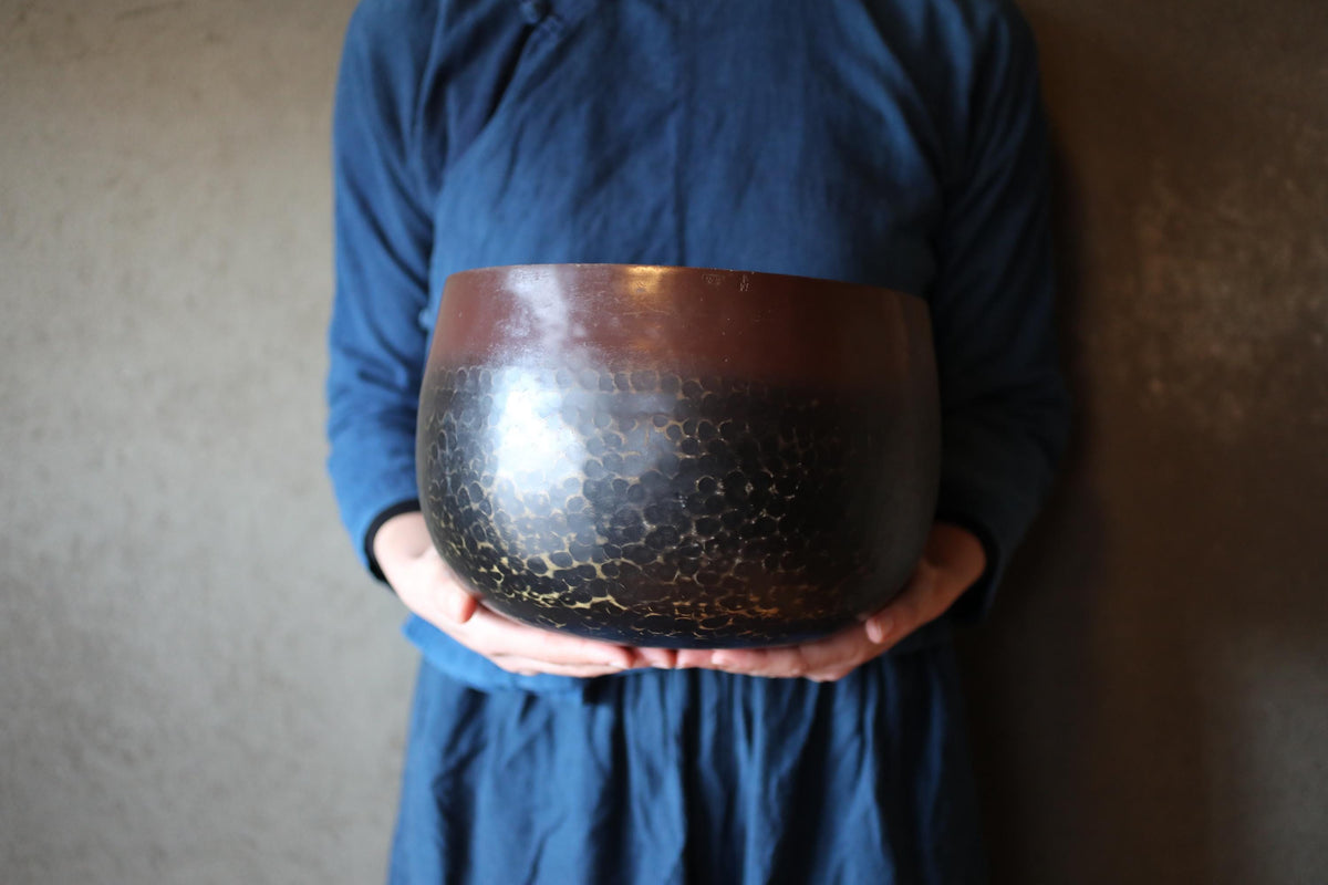 A person wearing a blue shirt is holding a large, round, brown and black bowl in their hands.