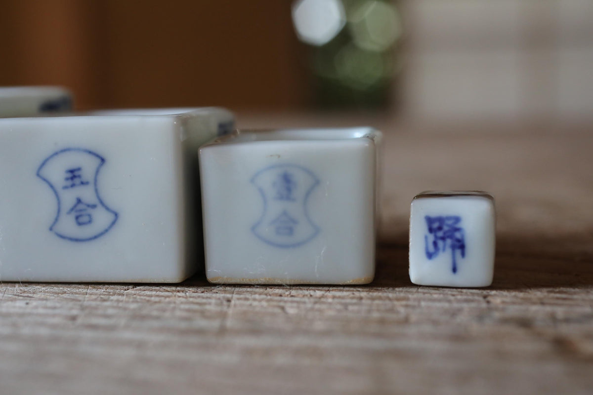 three white porcelain objects with blue designs, including a small square object with a blue design on it, placed on a wooden surface.