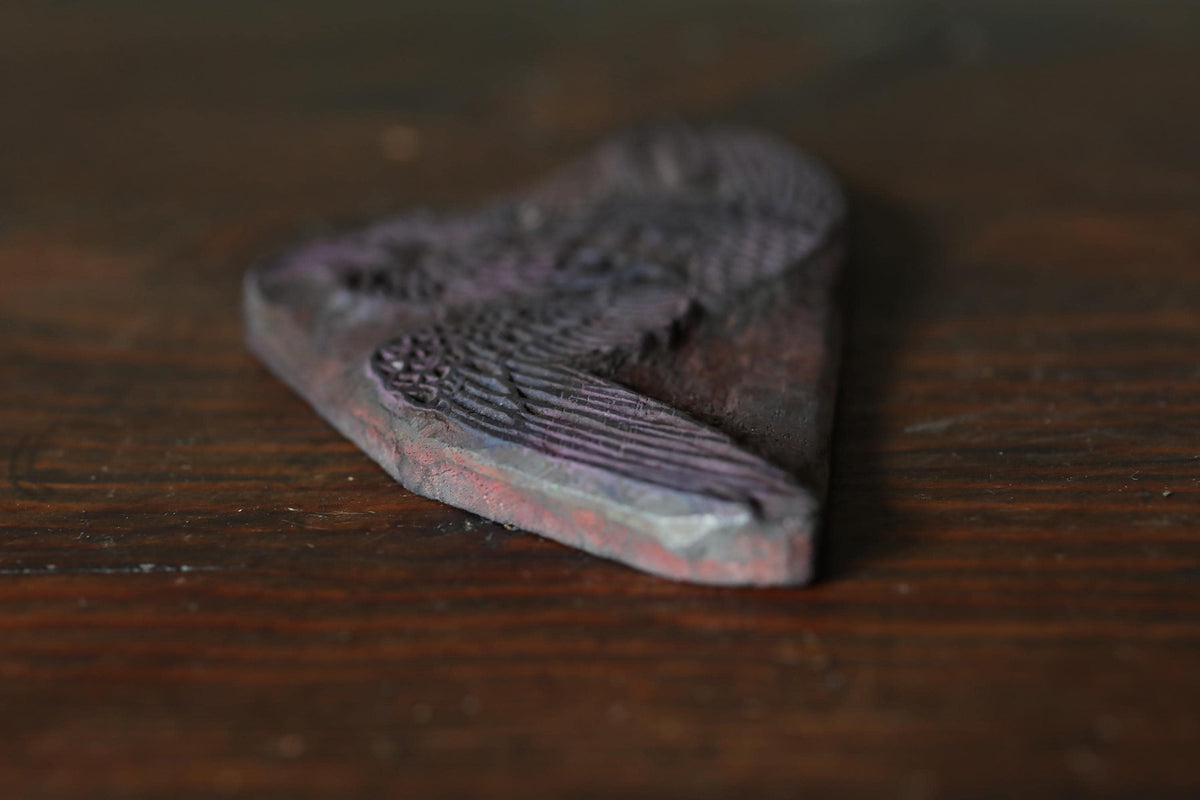 A close-up image of a dark-colored, textured object, possibly a piece of wood or a metal, resting on a wooden surface.