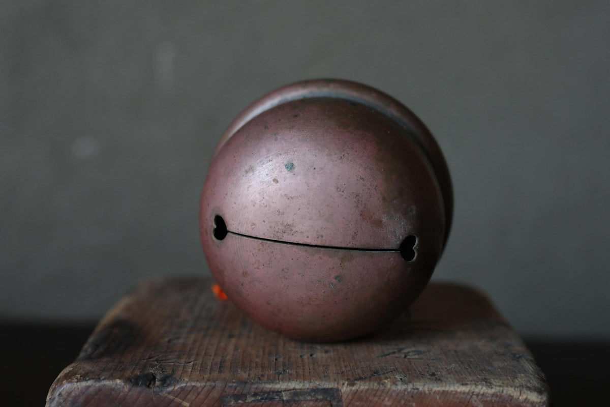 A round, metallic bell with a heart-shaped hole in the center, sitting on a wooden surface.