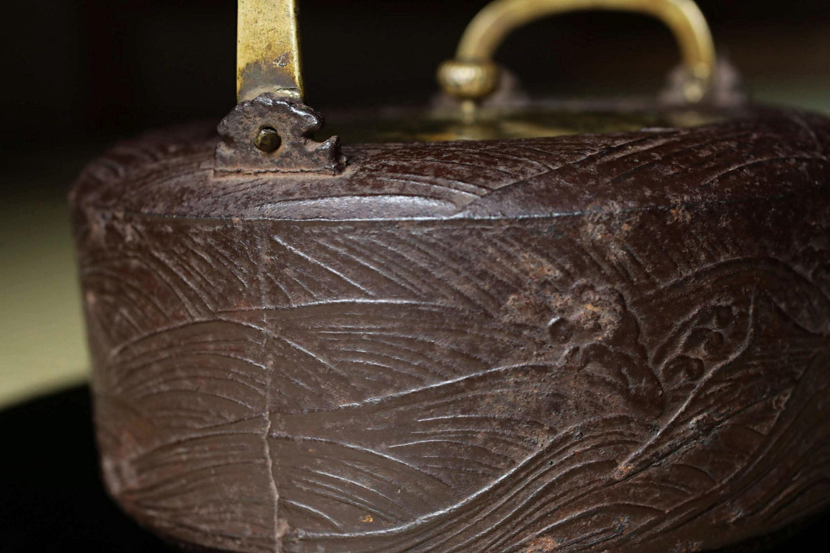 A close-up image of a dark brown, antique-looking metal object with a textured, engraved surface.