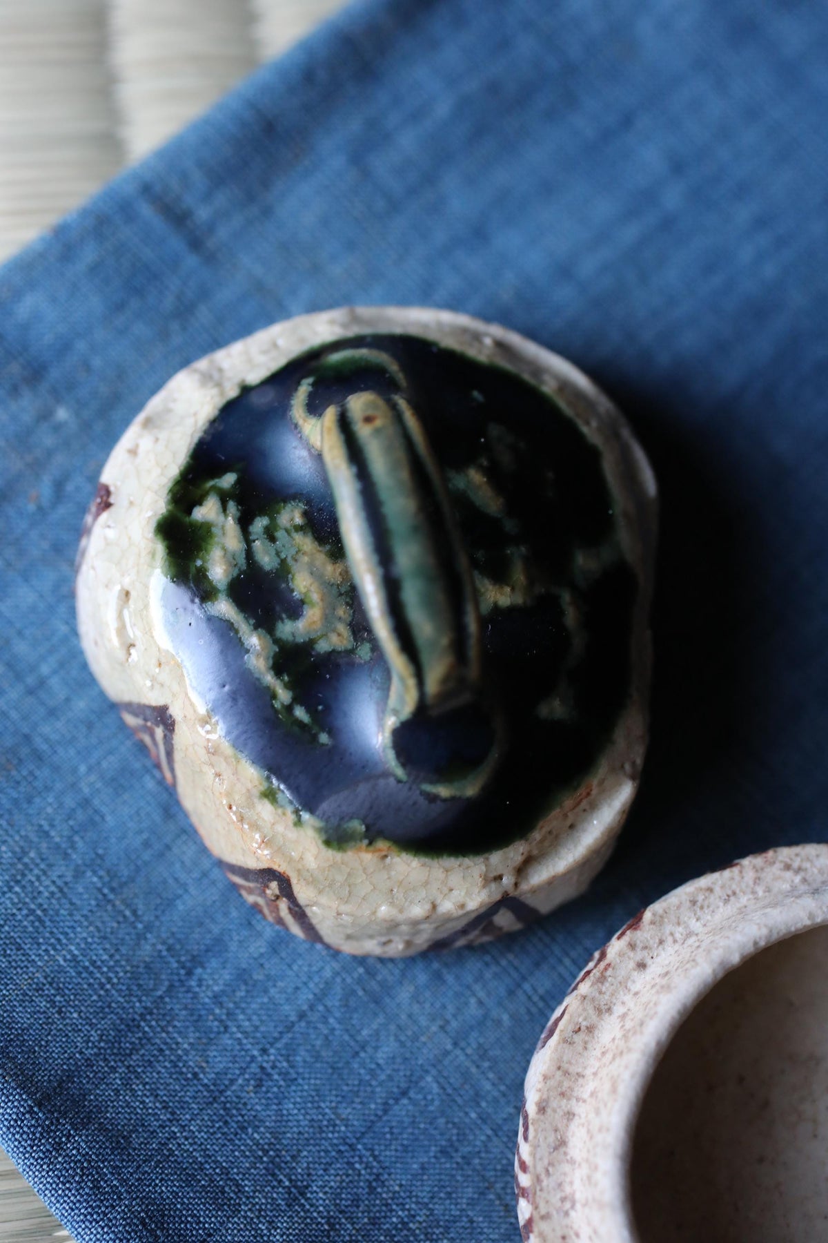 a ceramic object with a dark blue glaze and a lighter blue glaze, resting on a blue cloth.