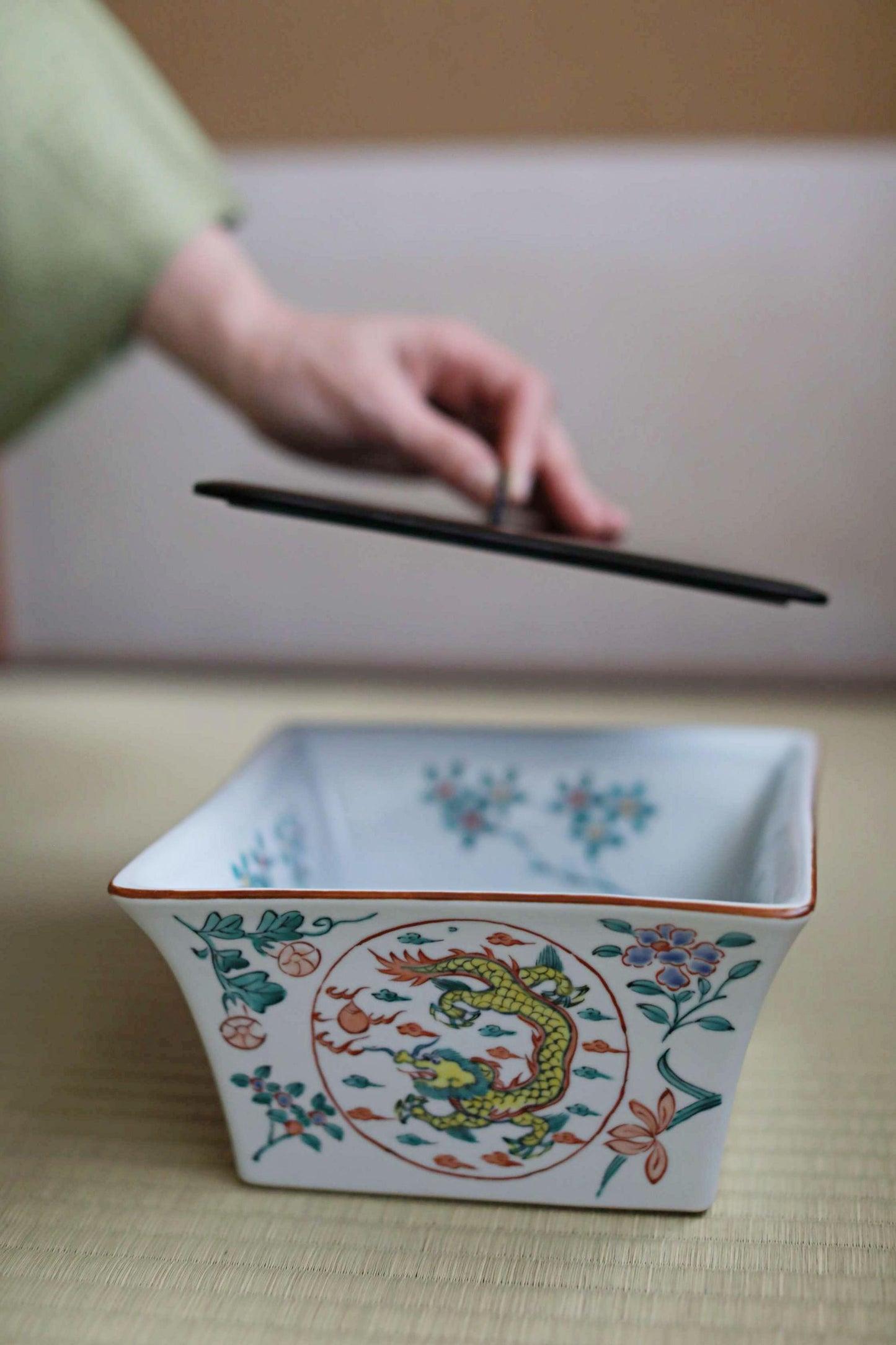 A hand is holding a black object above a white ceramic bowl with colorful floral designs.