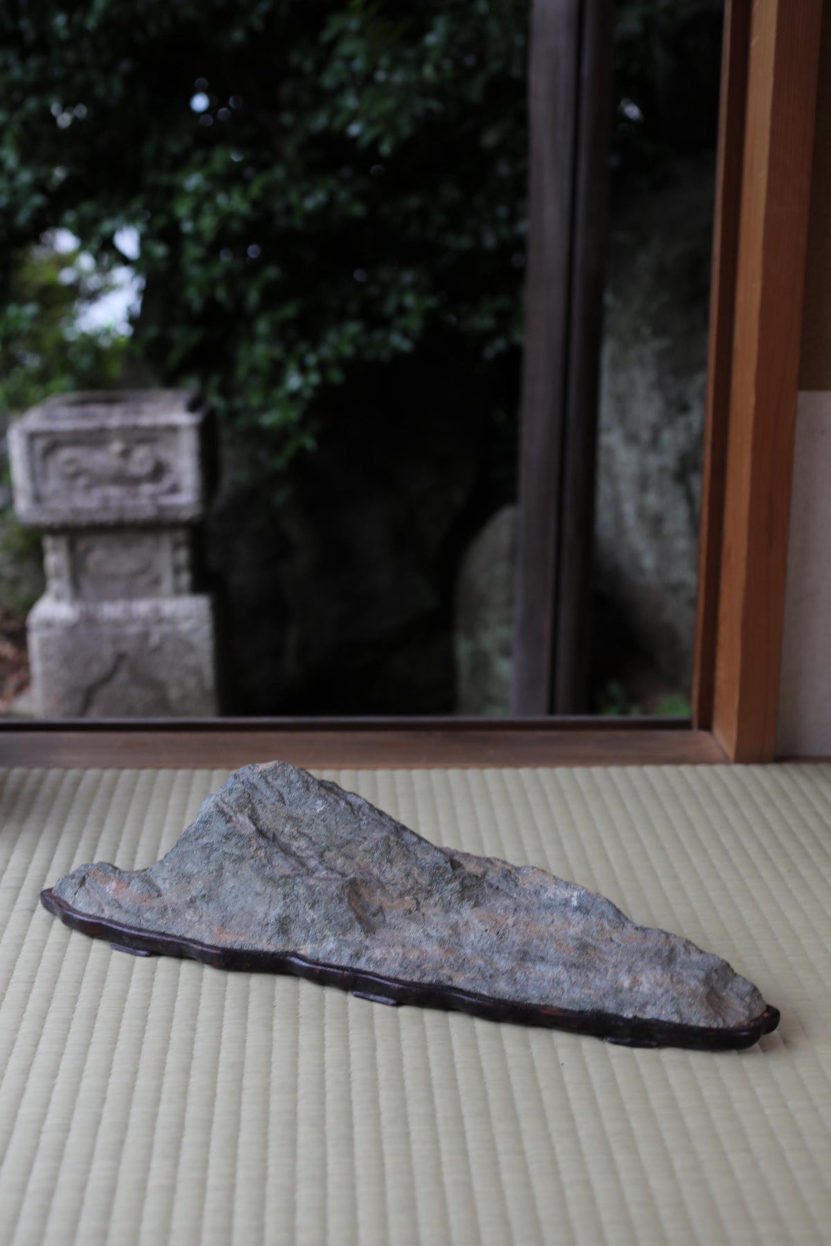 A large gray rock sits on a beige surface, with a stone structure visible in the background through a window.