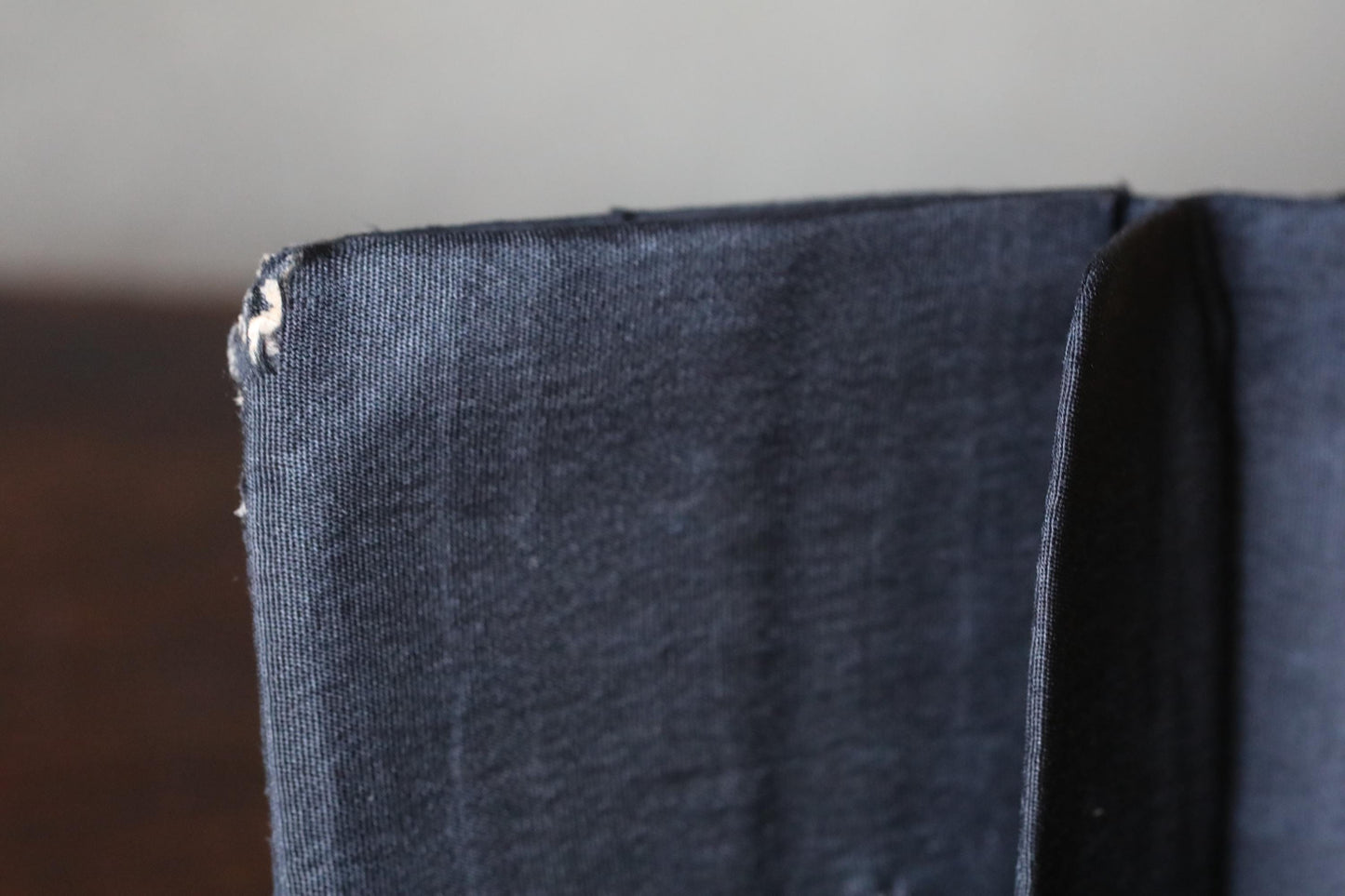 A close-up view of a dark fabric, possibly a piece of clothing or a textile, with a small tear or rip visible on the left side.