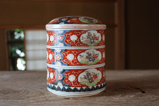A decorative ceramic container with a red and white pattern and floral designs, sitting on a wooden surface.