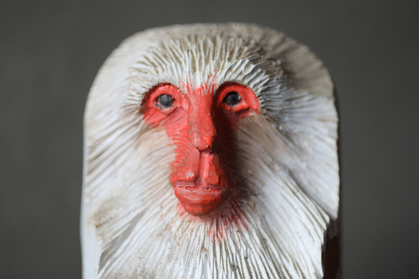 A close-up of a carved wooden sculpture depicting a white and red animal face, possibly a monkey or a bird.