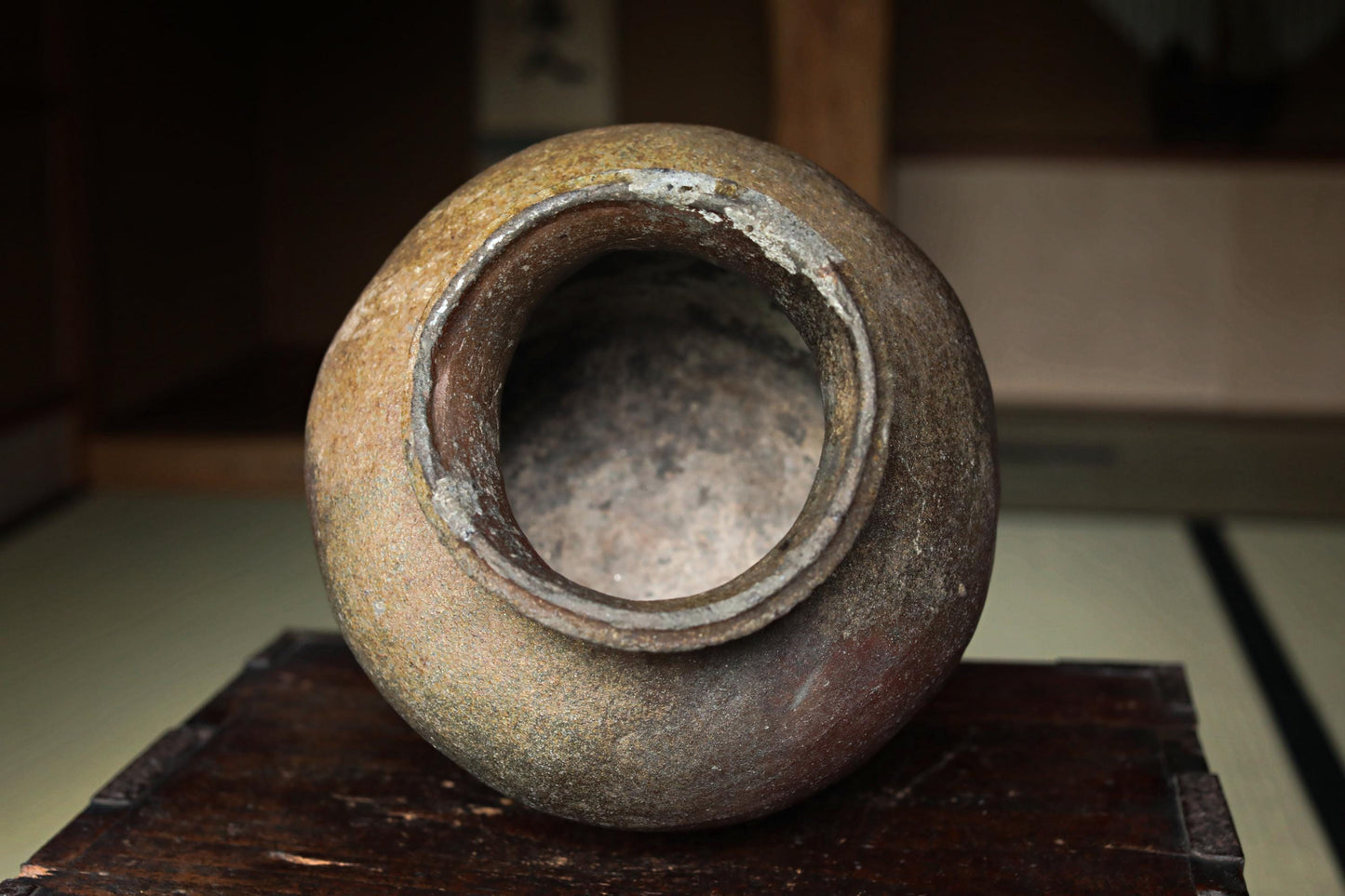 An old, weathered ceramic vase with a large opening in the center, sitting on a wooden surface.