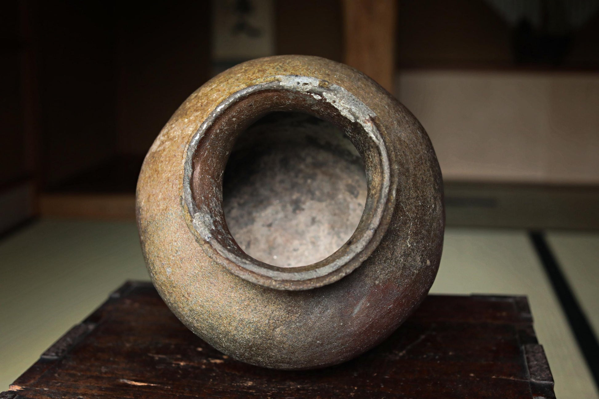 An old, weathered ceramic vase with a large opening in the center, sitting on a wooden surface.