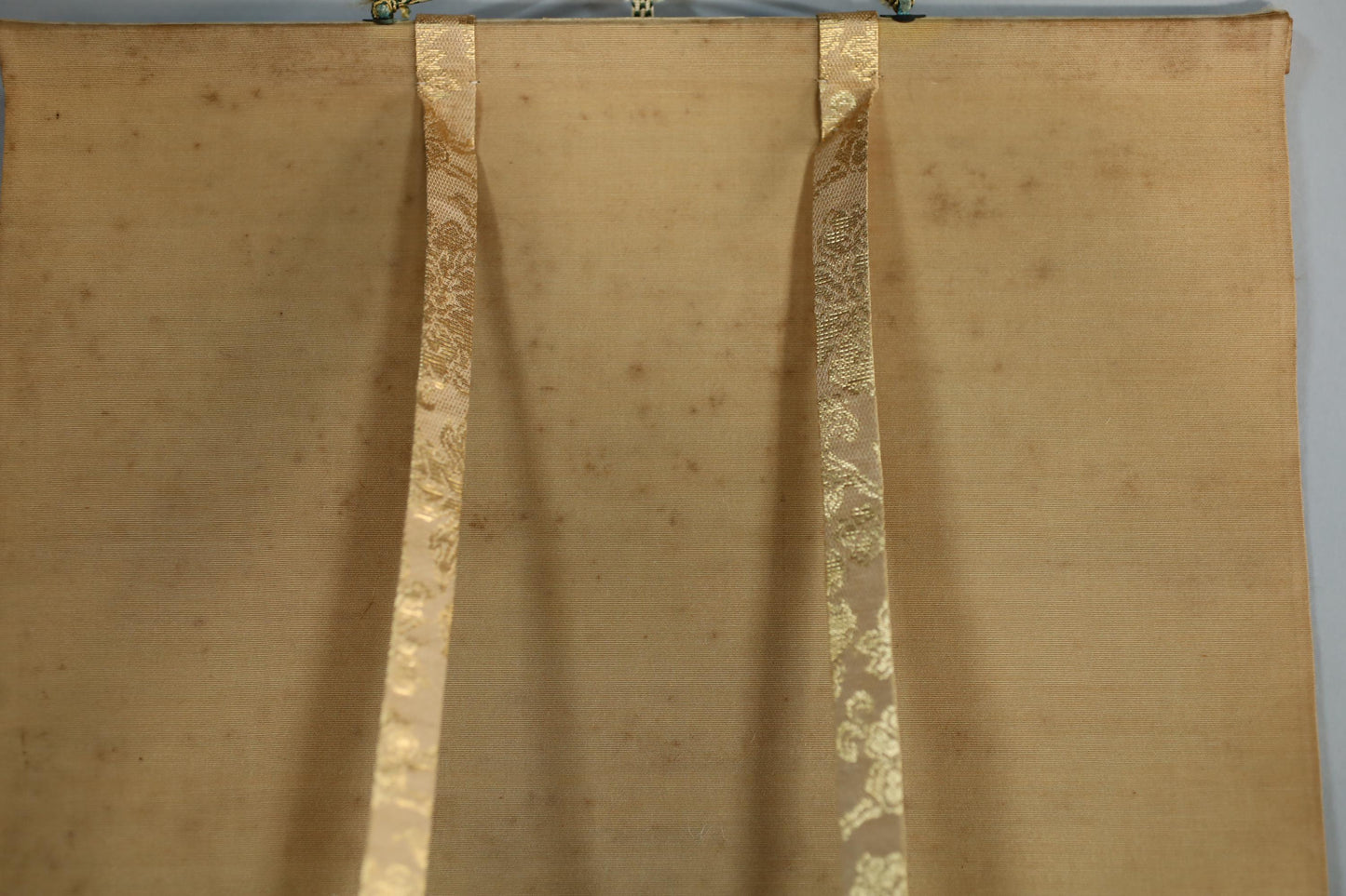 a close-up view of a beige fabric with a decorative pattern, featuring two gold-colored ribbons hanging from the fabric.
