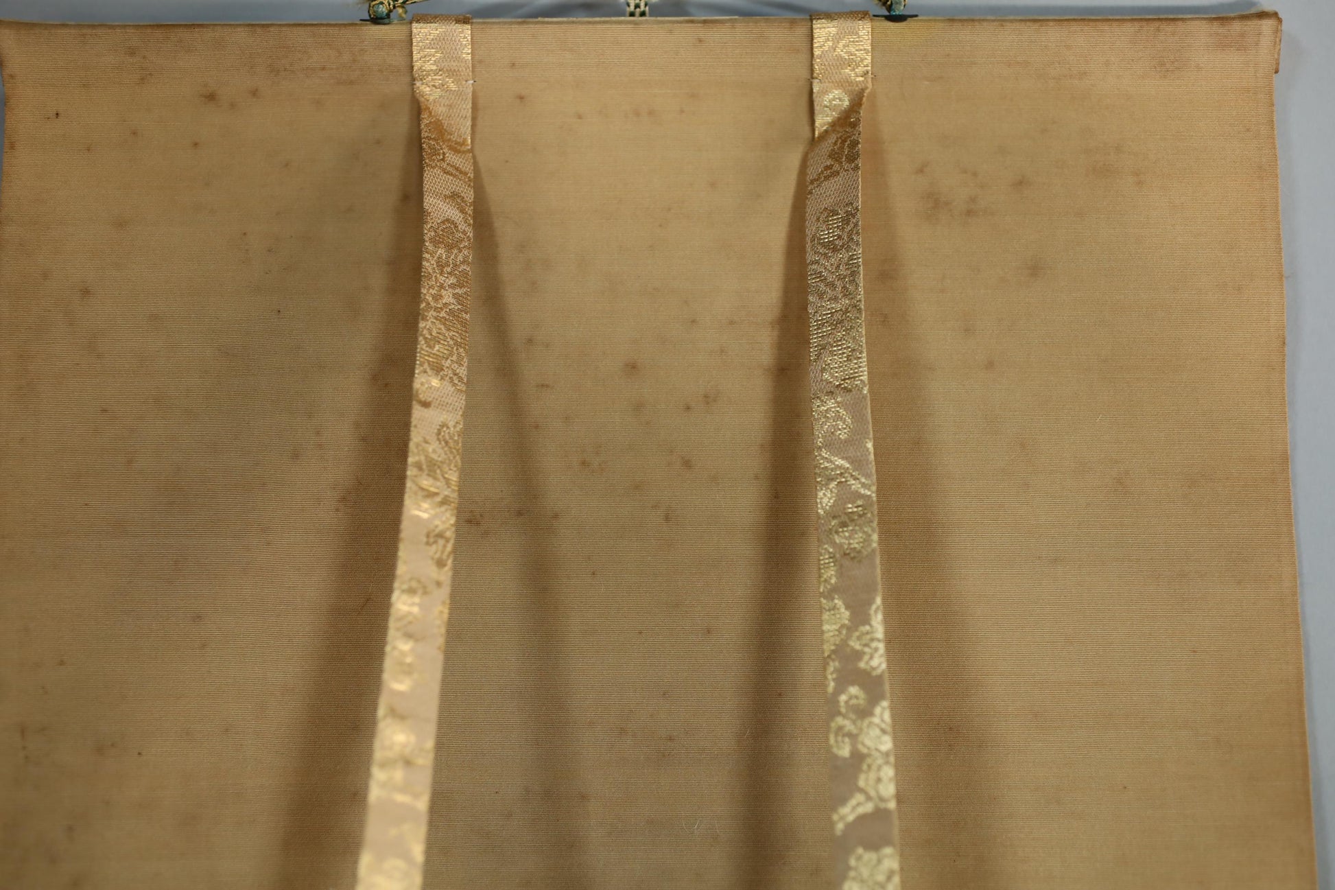a close-up view of a beige fabric with a decorative pattern, featuring two gold-colored ribbons hanging from the fabric.