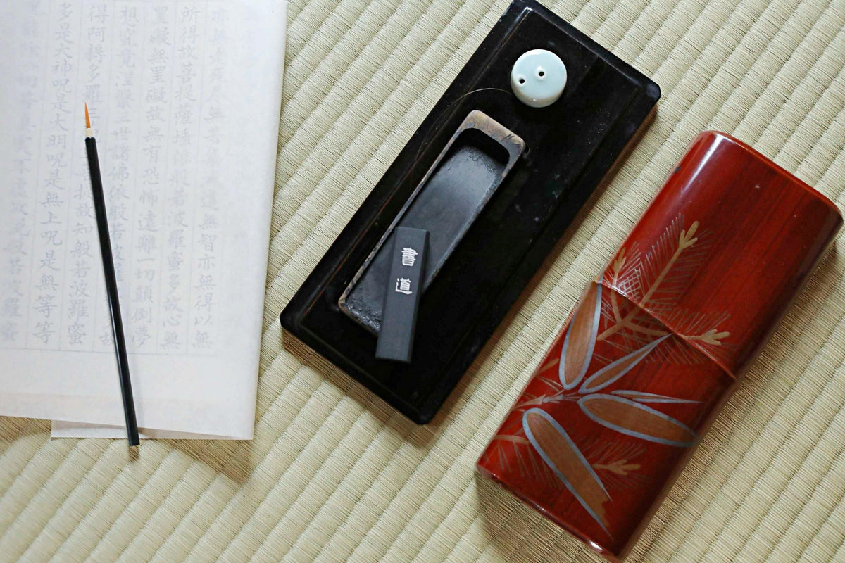a black tray with a pair of chopsticks and a red container with a floral design, all placed on a beige surface.