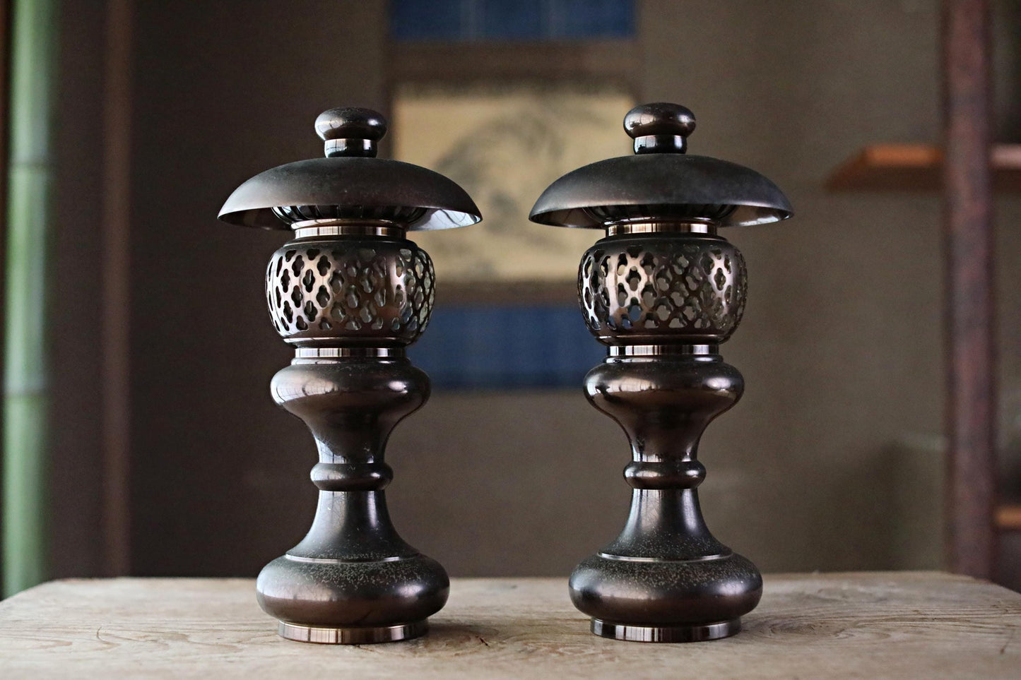 two ornate, black metal lanterns with intricate designs, placed side by side on a wooden surface.