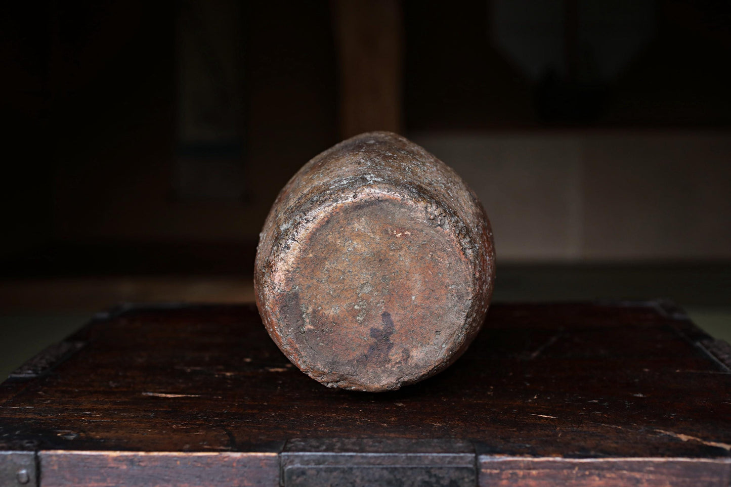 An old, rusted metal object, possibly a piece of machinery or tool, sits on a wooden surface in a dimly lit room.