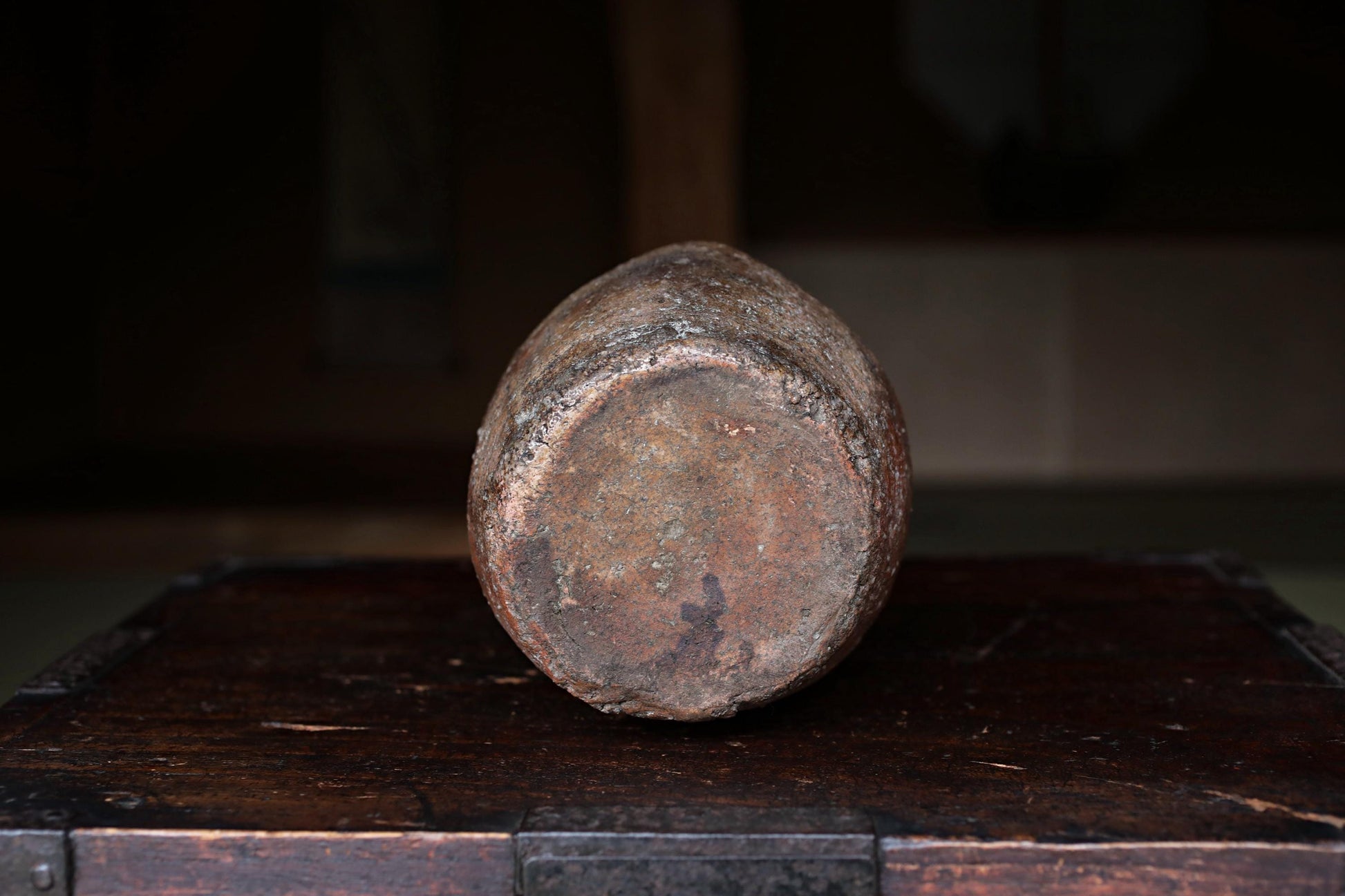 An old, rusted metal object, possibly a piece of machinery or tool, sits on a wooden surface in a dimly lit room.