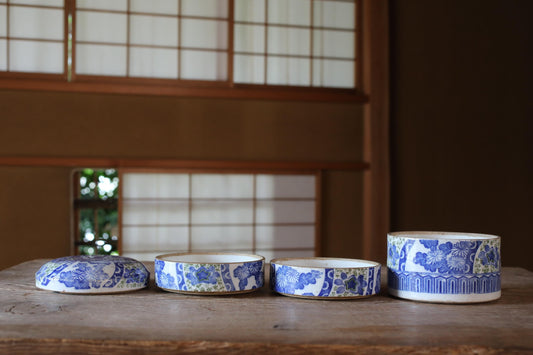 a collection of four blue and white ceramic bowls arranged on a wooden surface, with a window and wooden wall in the background.