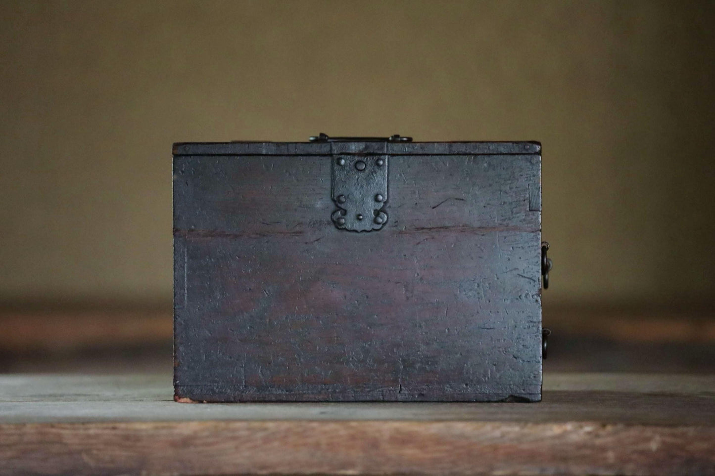 A dark wooden box with a metal latch on the top, sitting on a wooden surface.