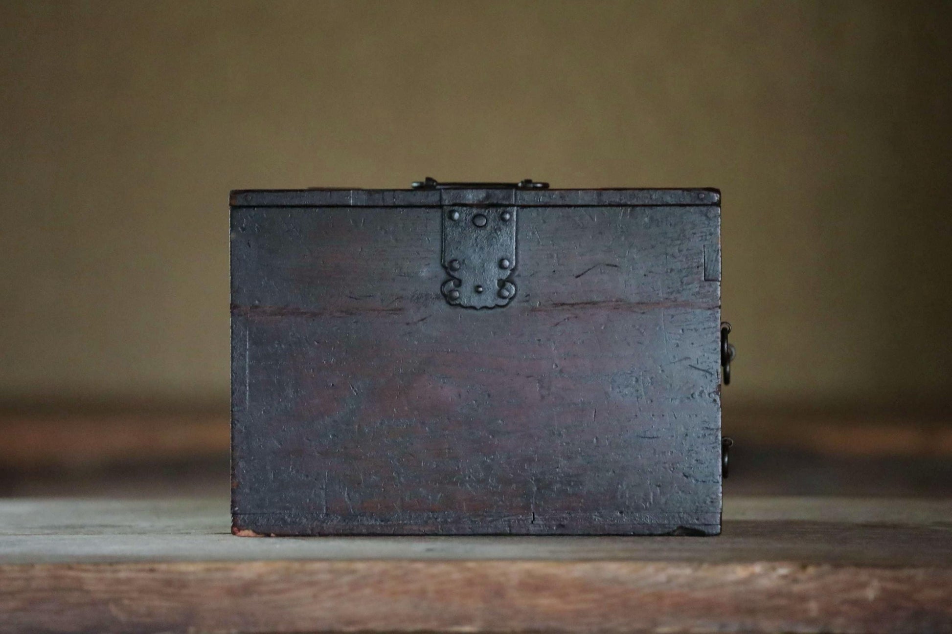 A dark wooden box with a metal latch on the top, sitting on a wooden surface.