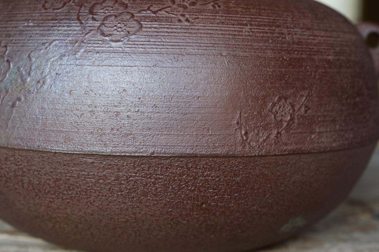 A close-up image of a dark brown ceramic bowl or vase with a floral design on its surface.