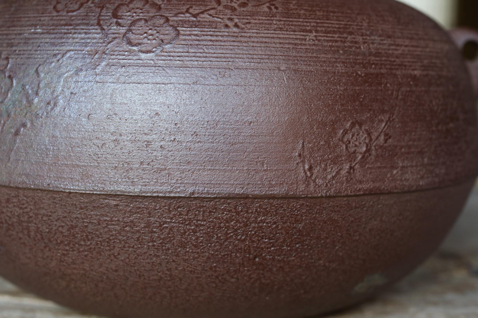A close-up image of a dark brown ceramic bowl or vase with a floral design on its surface.
