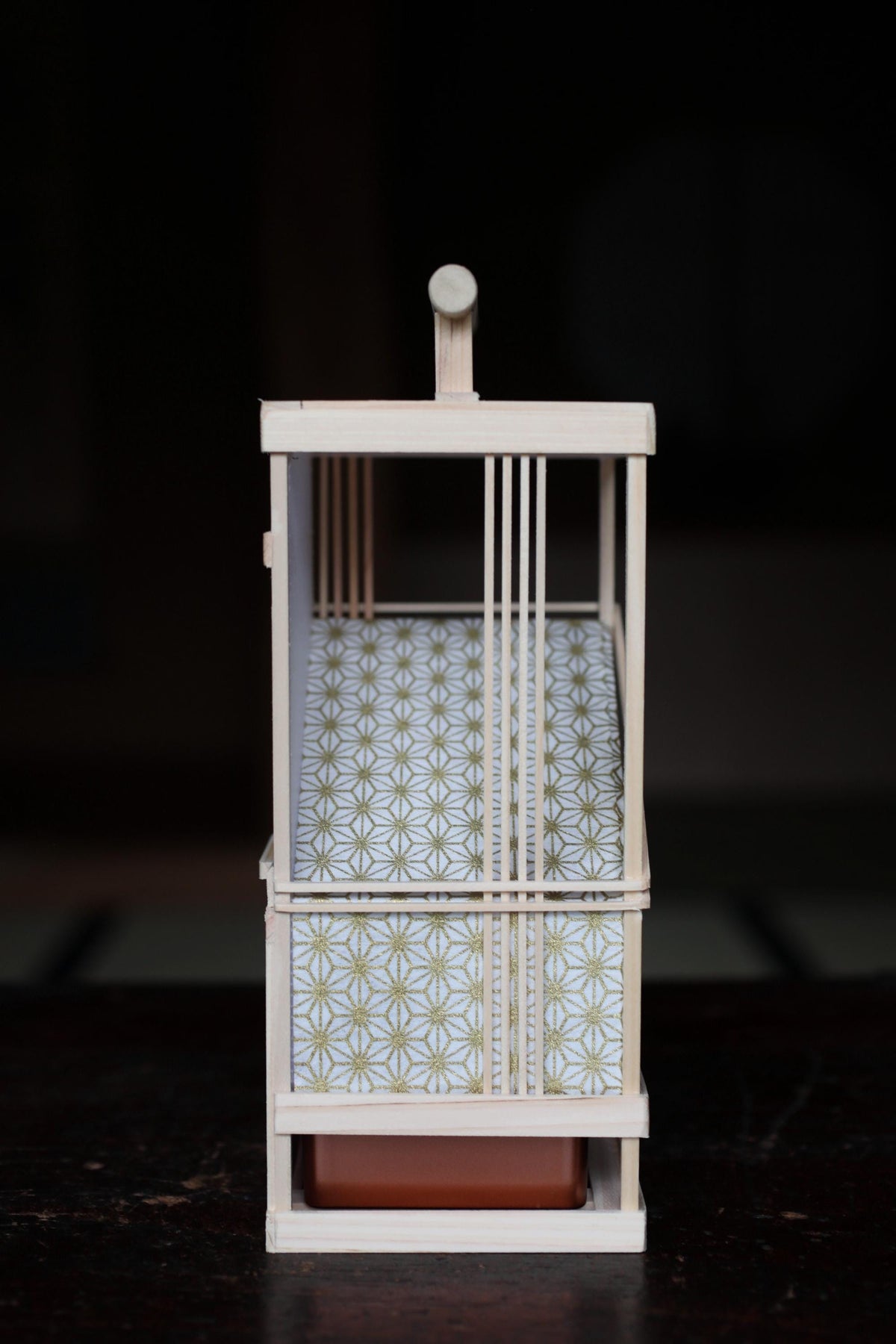 A small wooden birdcage with a white and gold patterned design, placed on a dark surface.