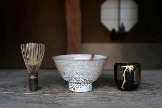 a wooden table with three objects on it: a wooden brush, a white bowl, and a black container.