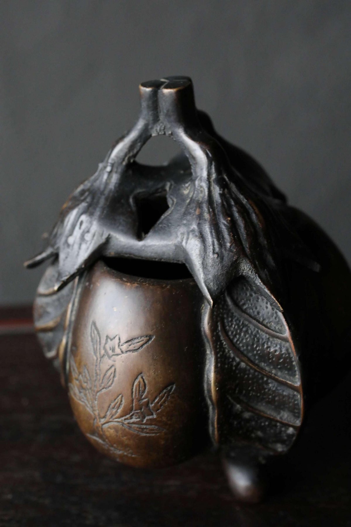A bronze vase with a leaf-like design on it, sitting on a dark surface.