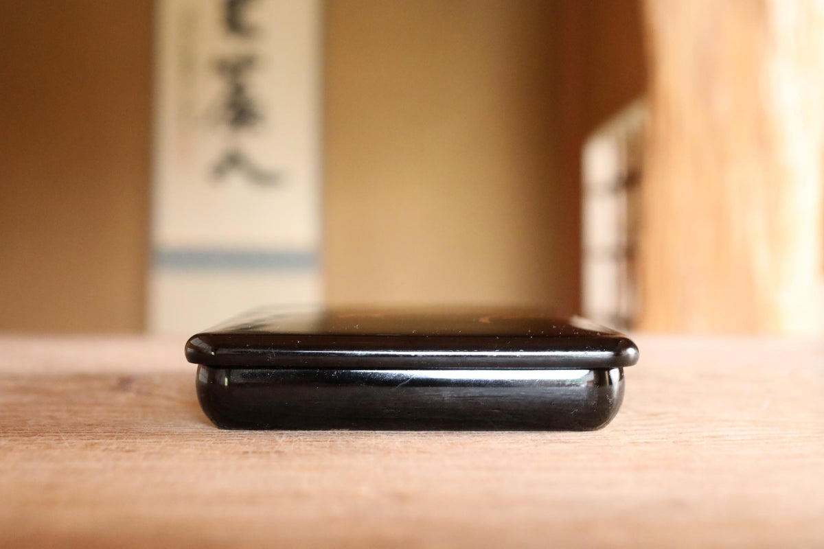 A black electronic device, possibly a smartphone or tablet, is sitting on a wooden surface.