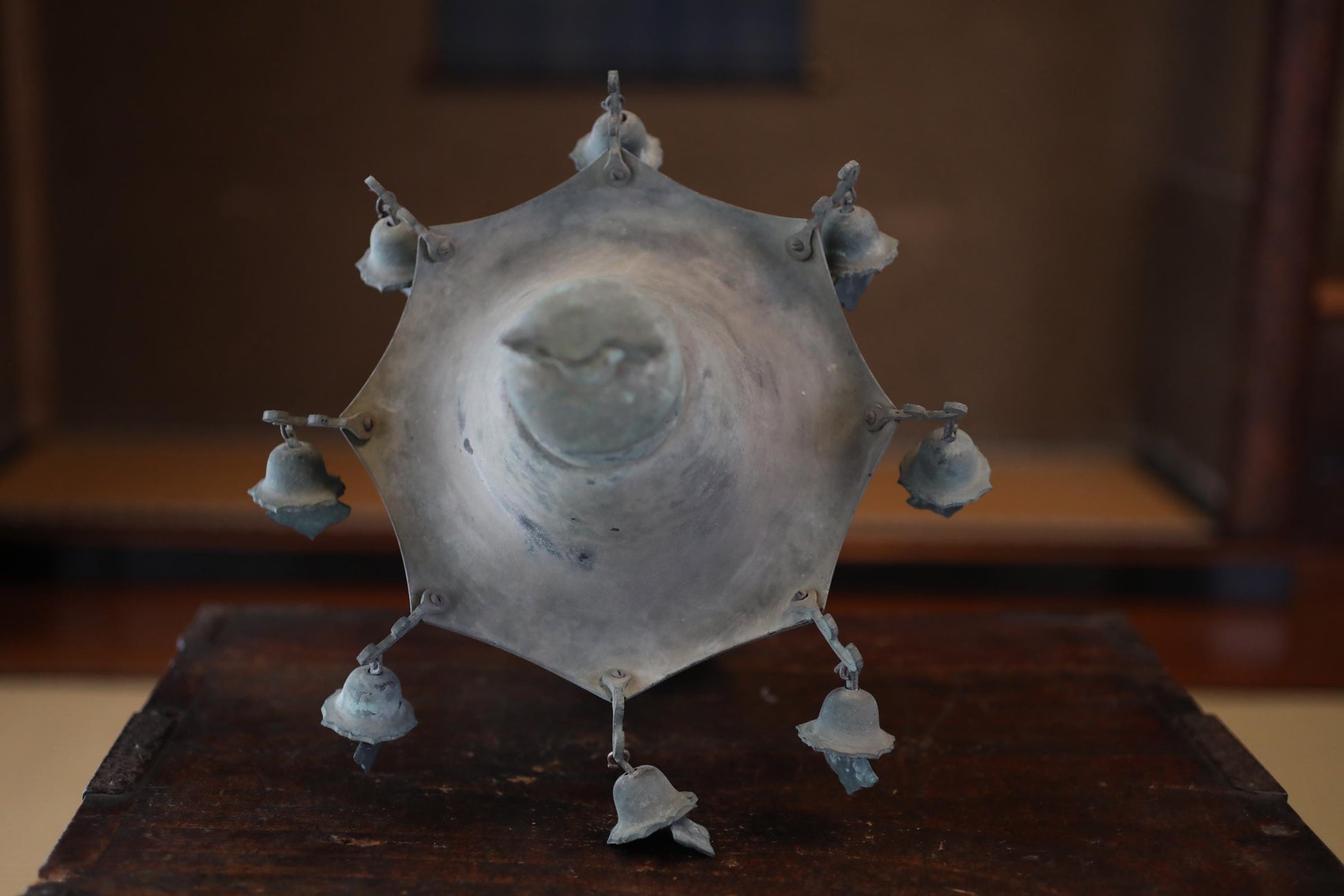 A metal bell-shaped object with multiple bells attached to it, displayed on a wooden surface.