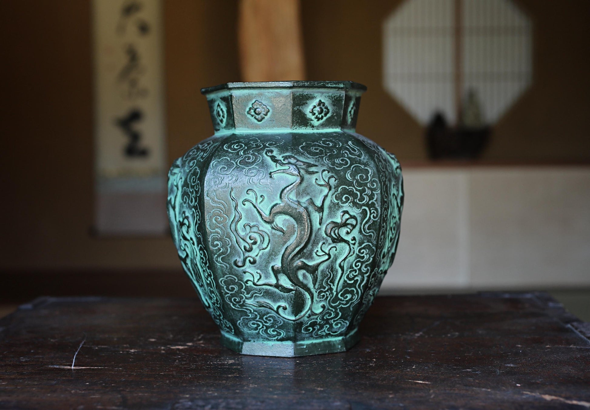 A decorative green vase with an intricate dragon design sits on a wooden surface.