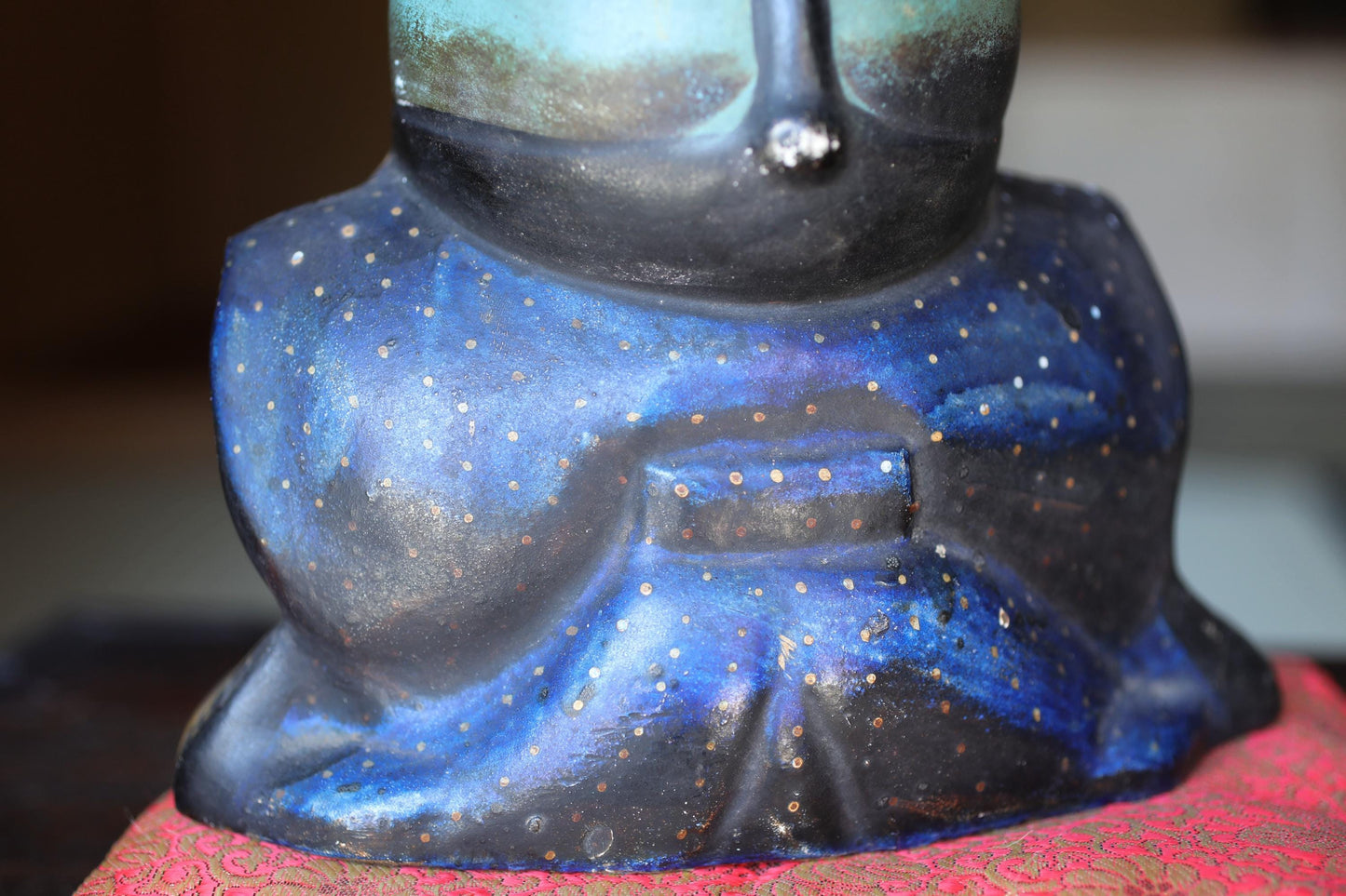 A close-up view of a blue and black ceramic sculpture with a starry pattern, sitting on a red and gold patterned surface.