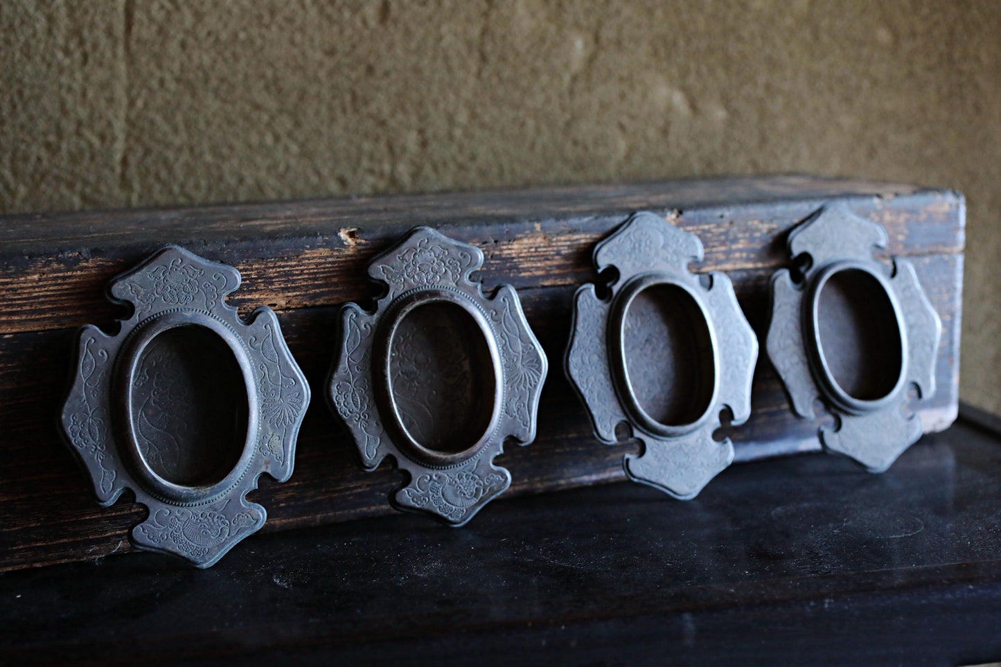 a wooden surface with four ornate metal frames arranged in a row, each with a circular opening.
