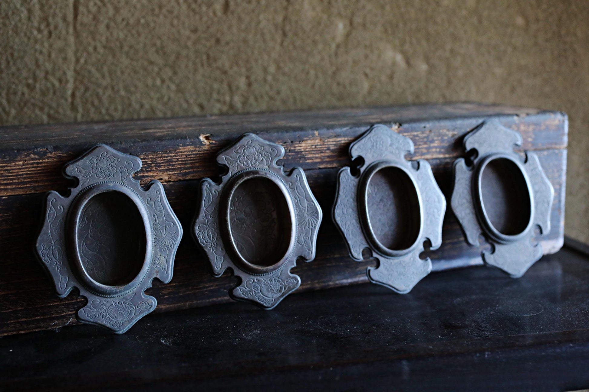 a wooden surface with four ornate metal frames arranged in a row, each with a circular opening.