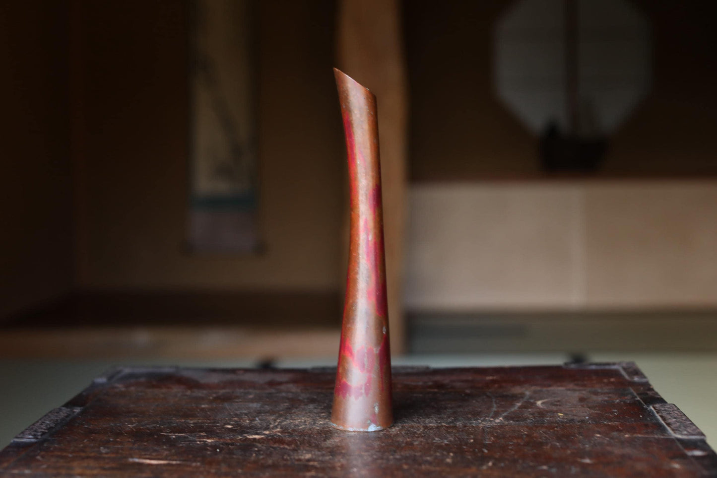 A tall, narrow vase with a red and orange color pattern sits on a wooden surface.