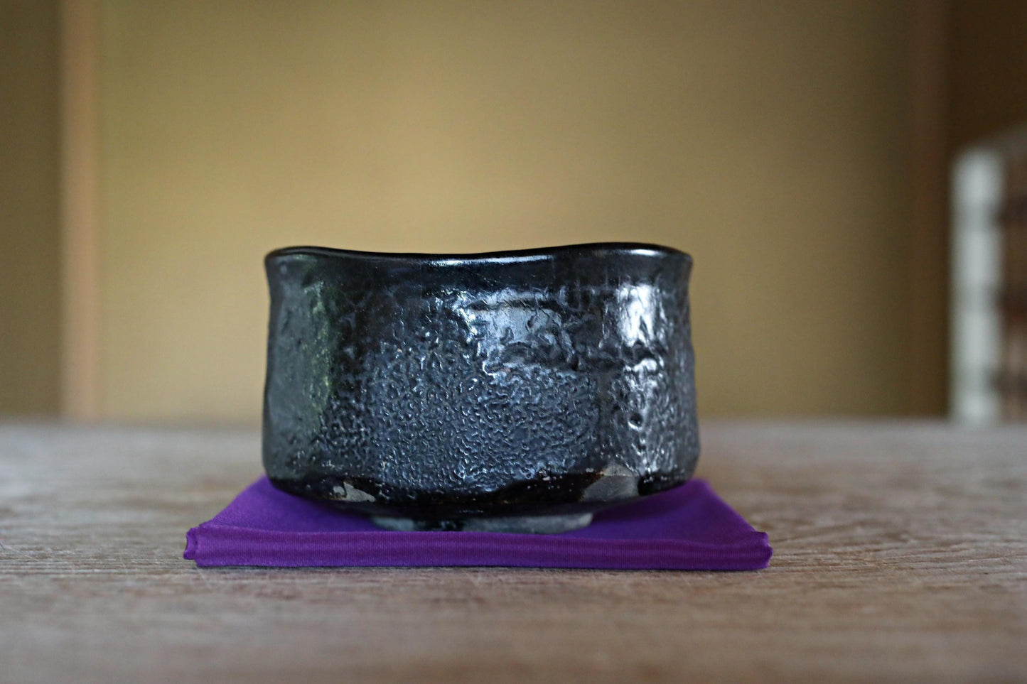 A black ceramic bowl with a textured surface sits on a purple cloth on a wooden surface.