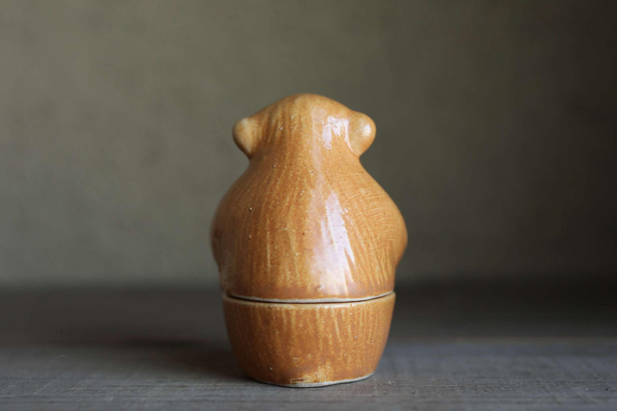 A ceramic figurine of a monkey sitting on a wooden surface.